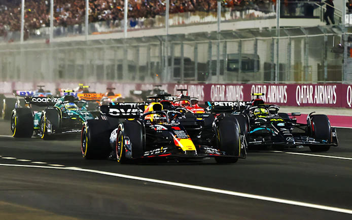 Race cars competing at F1 Qatar Grand Prix on a night track.
