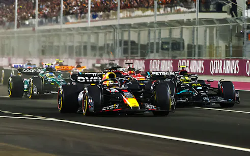 Race cars competing at F1 Qatar Grand Prix on a night track.