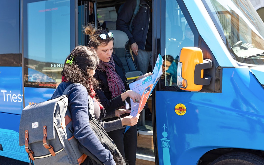 Passengers examining Hoptour map beside a blue tour bus.