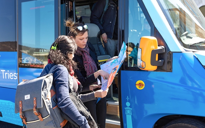 Passengers examining Hoptour map beside a blue tour bus.