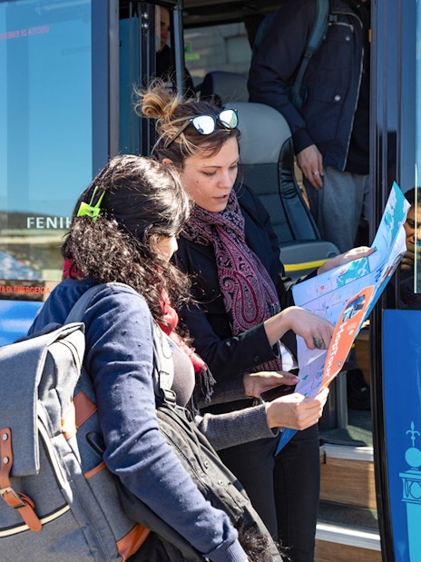 Passengers examining Hoptour map beside a blue tour bus.