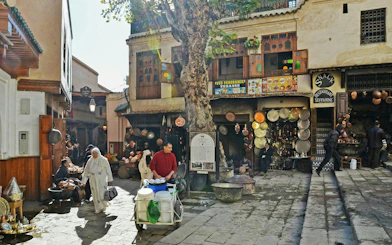 Fes Old Medina market scene with locals, copperware shops, and traditional architecture.