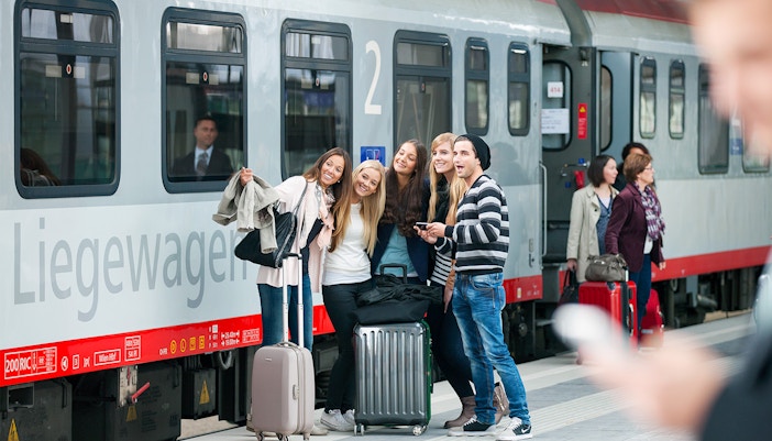 Travelers with Interrail Pass at a bustling European train station platform.