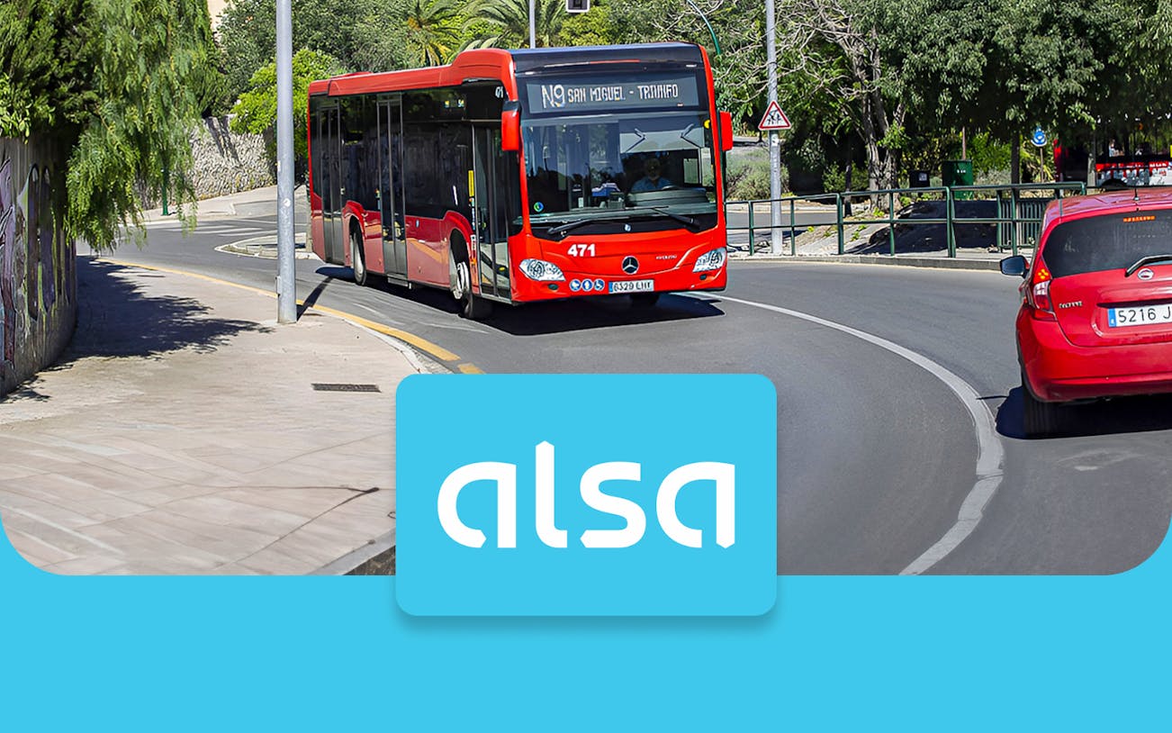 Red Alsa bus on a road in Granada, Spain, with Alsa logo in foreground.