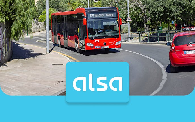 Red Alsa bus on a road in Granada, Spain, with Alsa logo in foreground.