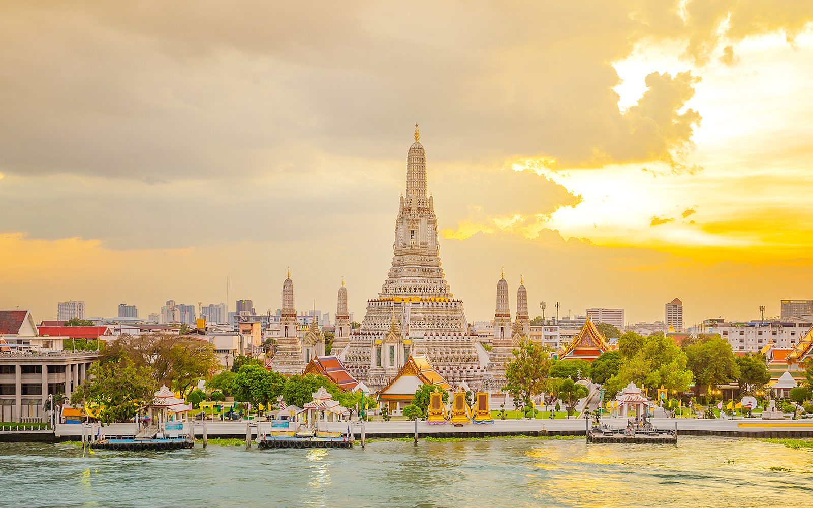 Wat Arun Temple in Bangkok at sunset with Chao Phraya River in the foreground.