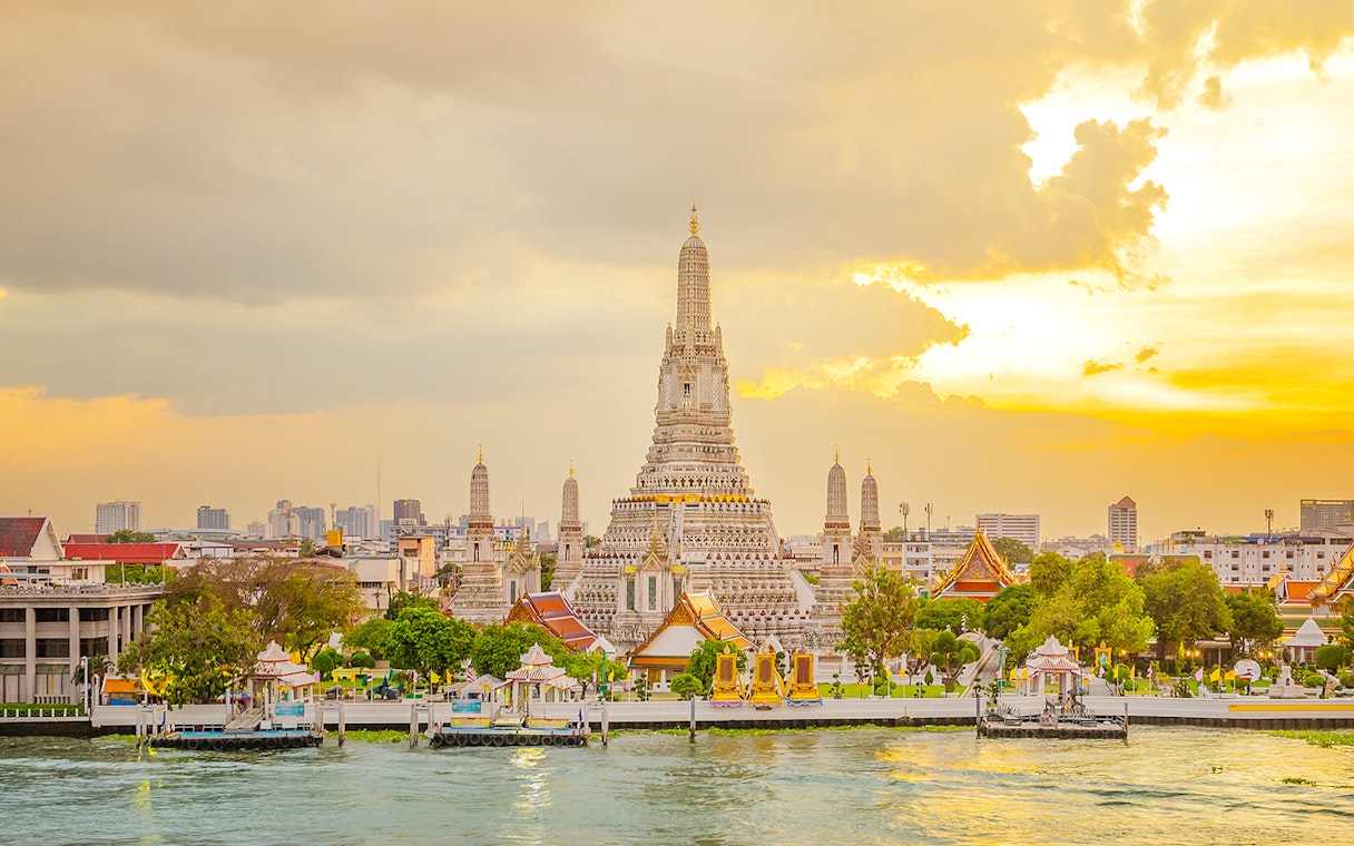Wat Arun Temple in Bangkok at sunset with Chao Phraya River in the foreground.