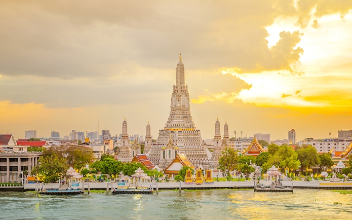 Wat Arun Temple in Bangkok at sunset with Chao Phraya River in the foreground.