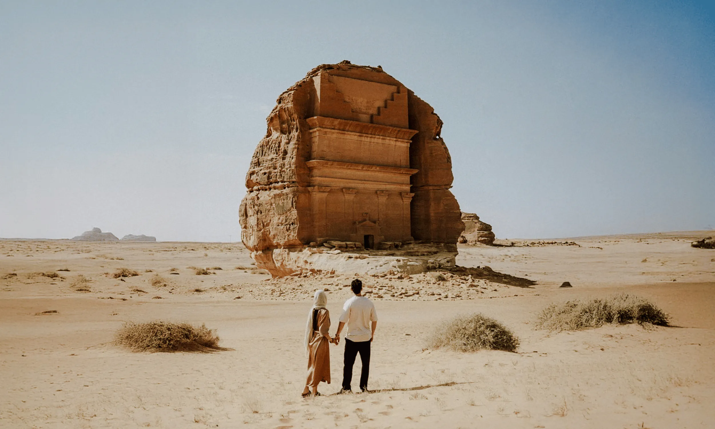 Couple viewing the ancient rock tomb of Hegra in AlUla, Saudi Arabia desert.