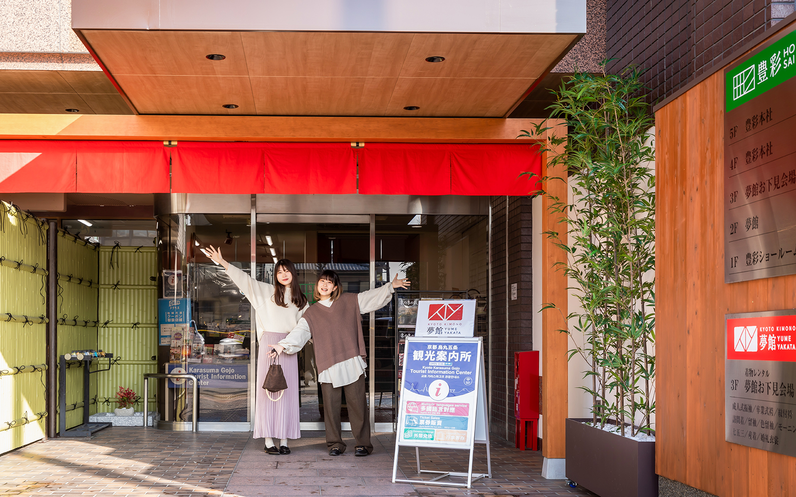 Guests at Kyoto Kimono Rental entrance, posing with arms raised.