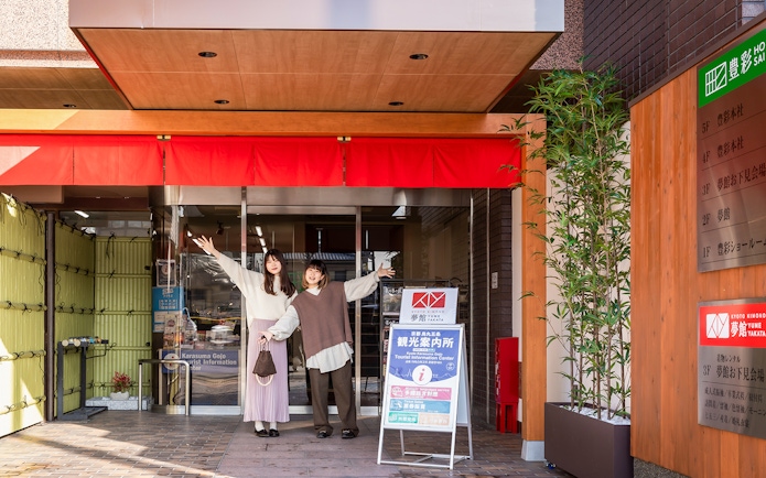 Guests at Kyoto Kimono Rental entrance, posing with arms raised.