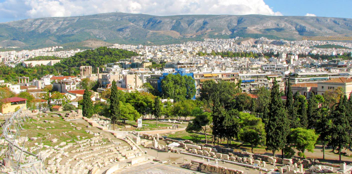 Theatre and Sanctuary of Dionysus in Athens with cityscape and mountains in the background.