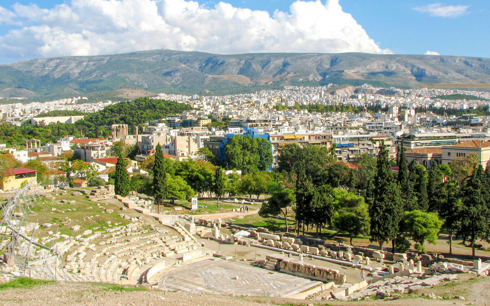 Theatre and Sanctuary of Dionysus in Athens with cityscape and mountains in the background.