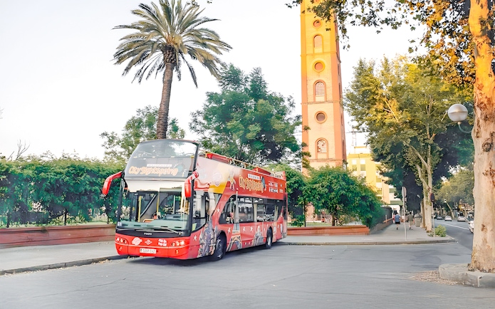 Seville hop-on hop-off tour bus near historic tower and palm trees.