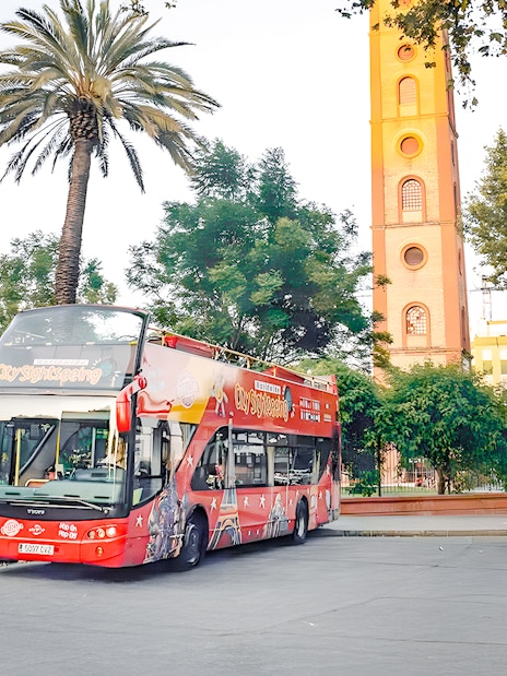 Seville hop-on hop-off tour bus near historic tower and palm trees.