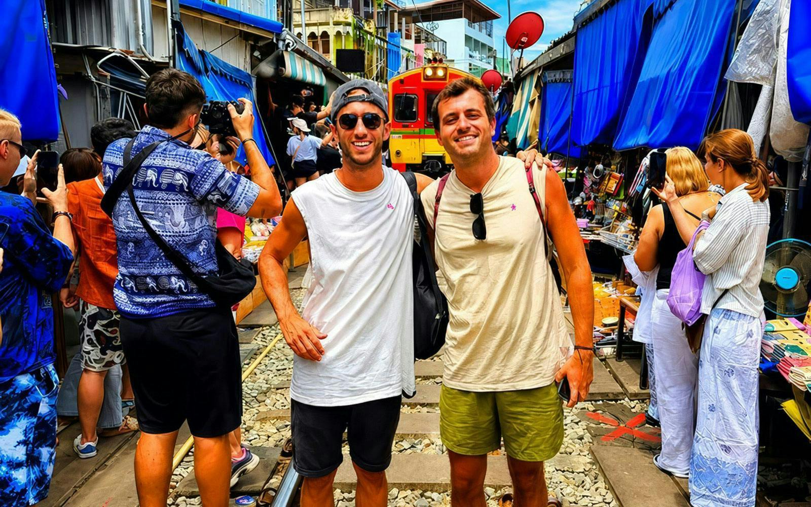 Tourists at Maeklong Train Market in Bangkok with train approaching.