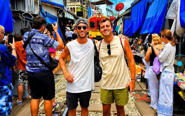 Tourists at Maeklong Train Market in Bangkok with train approaching.