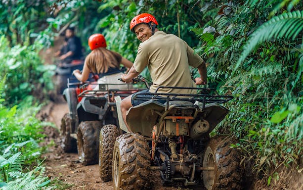 Man smiling while riding ATV through lush forest trail.