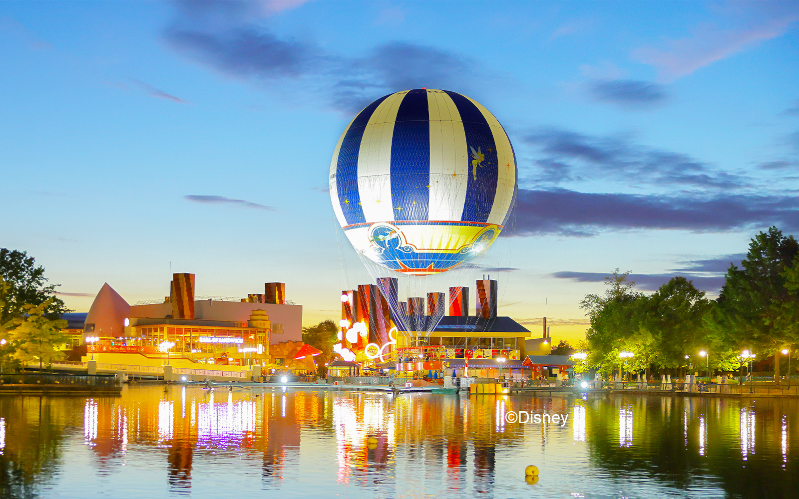 Hot air balloon over Disney Village at sunset, reflecting on the water.