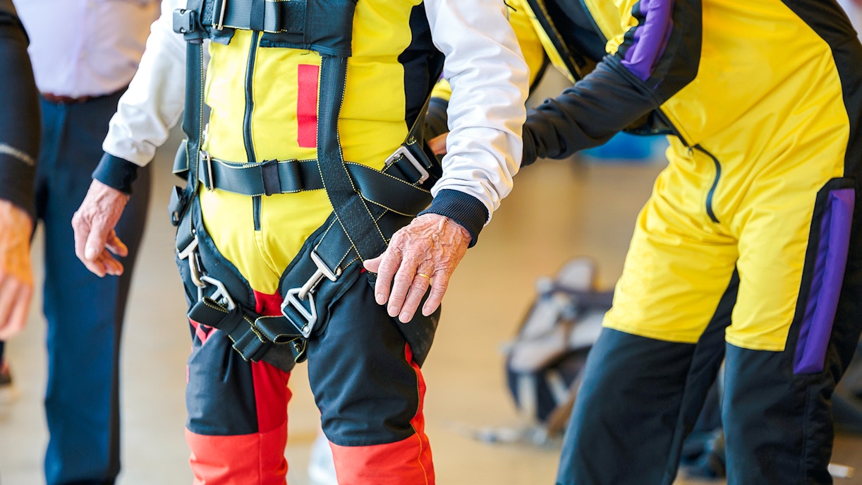 Person inspecting skydiving harness and gear indoors.