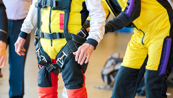 Person inspecting skydiving harness and gear indoors.