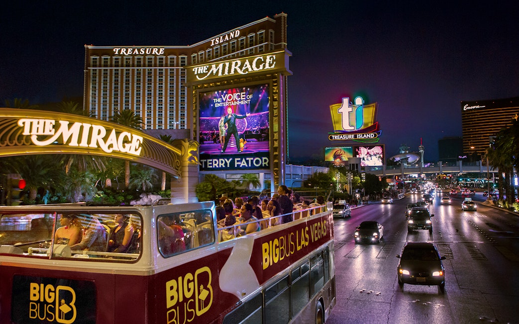 Open-top bus tour passing The Mirage and Treasure Island in Las Vegas at night.