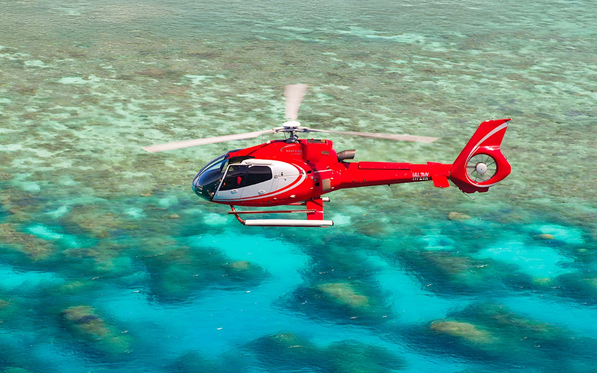 Red helicopter flying over the Great Barrier Reef's turquoise waters.
