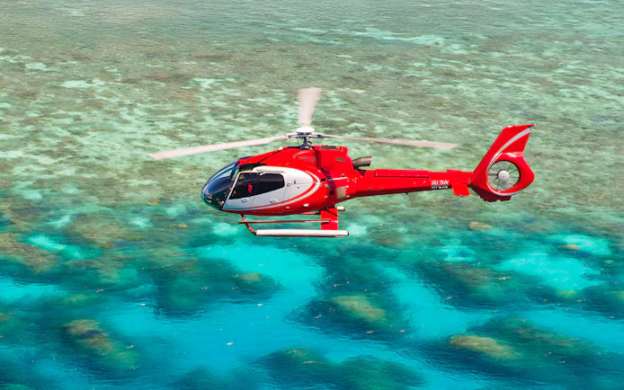 Red helicopter flying over the Great Barrier Reef's turquoise waters.