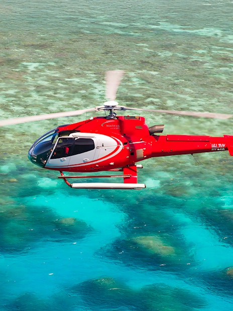 Red helicopter flying over the Great Barrier Reef's turquoise waters.