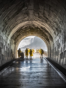 Visitors in yellow ponchos walking through Niagara Falls Tunnel towards the waterfall.