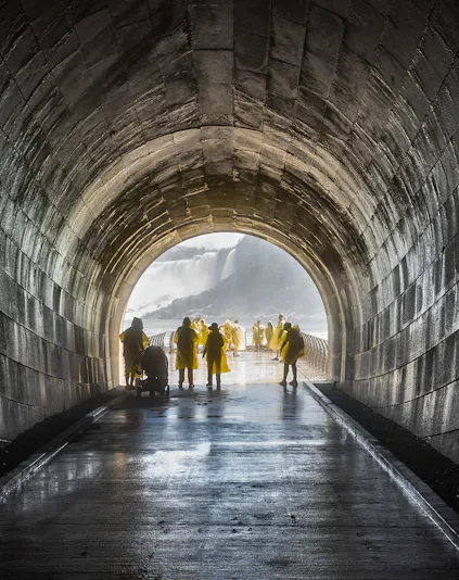 Visitors in yellow ponchos walking through Niagara Falls Tunnel towards the waterfall.