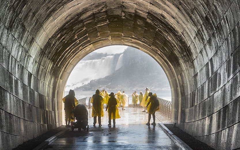 Visitors in yellow ponchos walking through Niagara Falls Tunnel towards the waterfall.