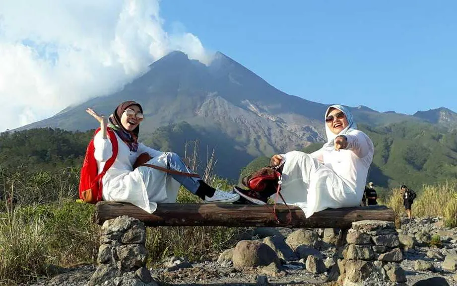 Two people sitting on a bench with Mount Merapi in the background during a Jeep Merapi Lava Tour.