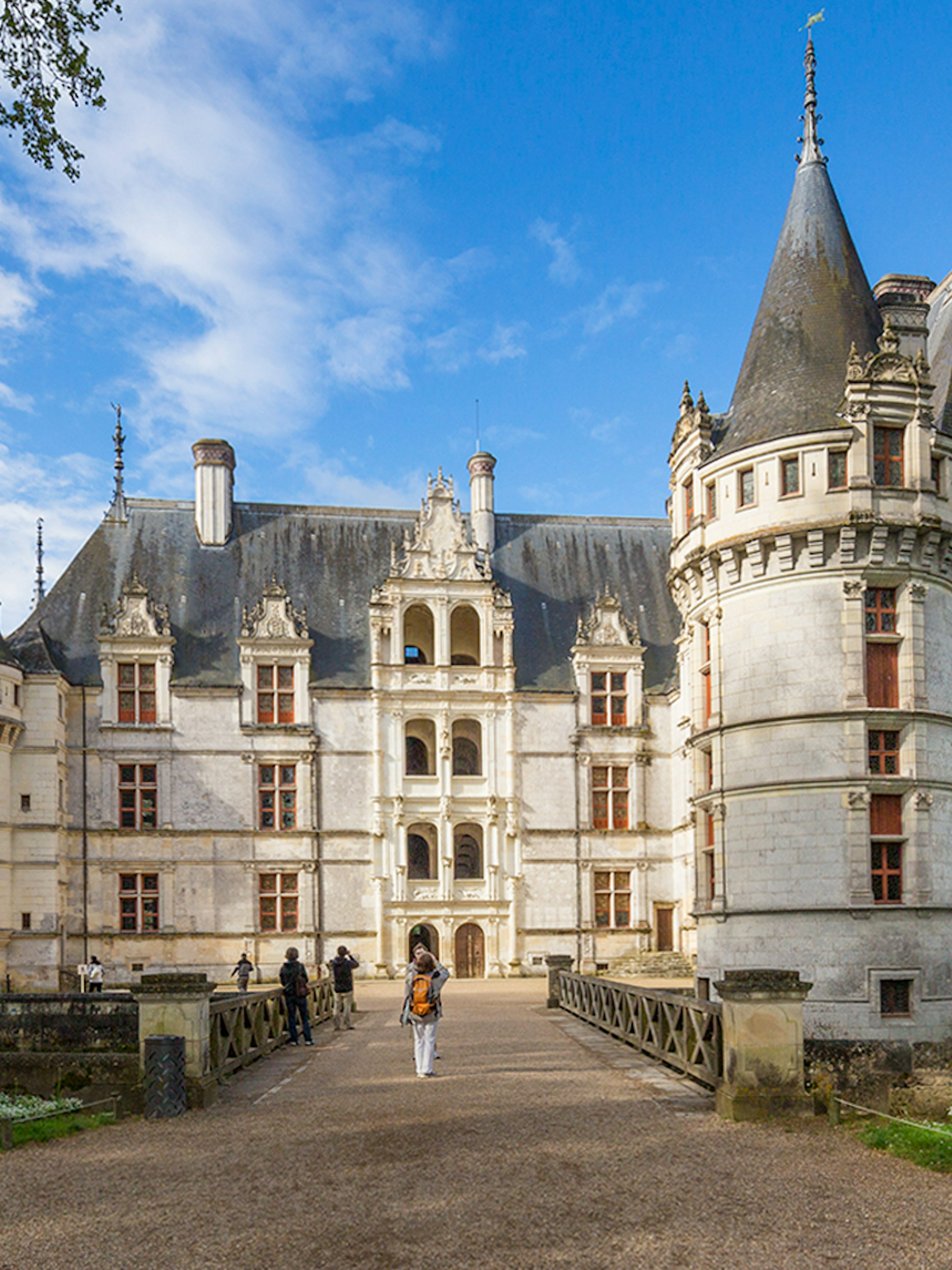 Chateau d'Azay-le-Rideau with visitors walking on the path, surrounded by gardens and trees.