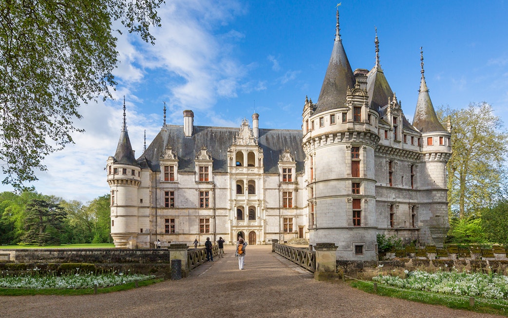 Chateau d'Azay-le-Rideau with visitors walking on the path, surrounded by gardens and trees.