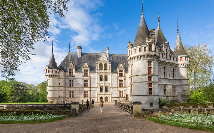 Chateau d'Azay-le-Rideau with visitors walking on the path, surrounded by gardens and trees.