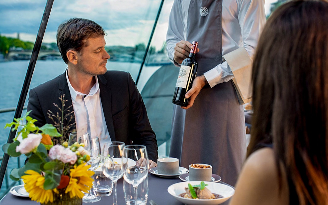 Server presenting wine to guests on a Seine River dinner cruise.