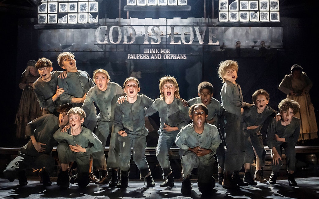Children performing on stage in a scene from the musical Oliver!