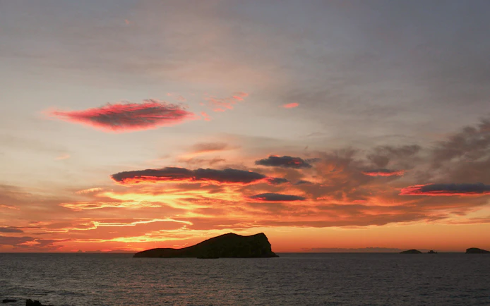 Sunset over Cala Bassa Beach with vibrant clouds in Ibiza, Spain.