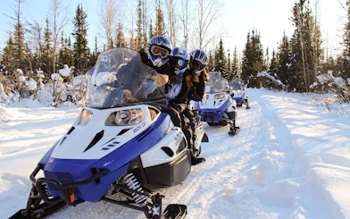 Snowmobile riders on a snowy trail in Fairbanks, Alaska forest.
