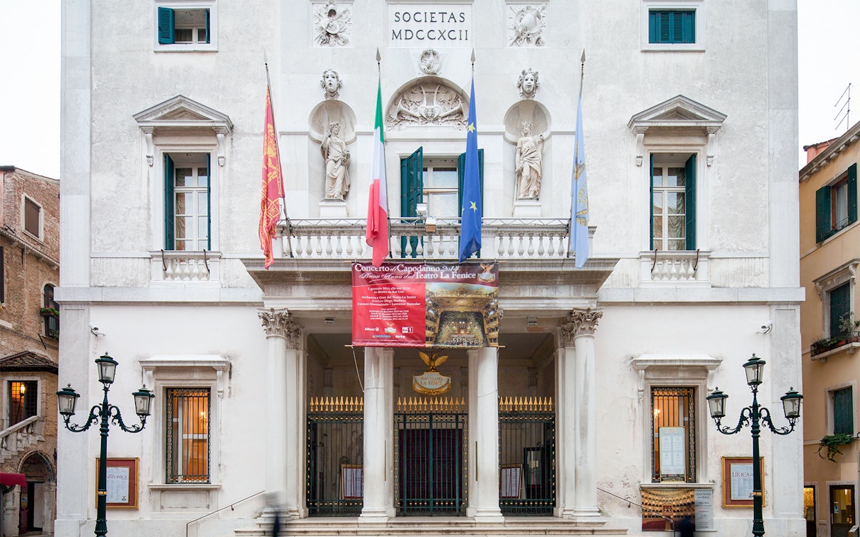 Facade of Teatro La Fenice in Venice, Italy, with flags and statues.