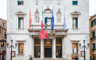 Facade of Teatro La Fenice in Venice, Italy, with flags and statues.