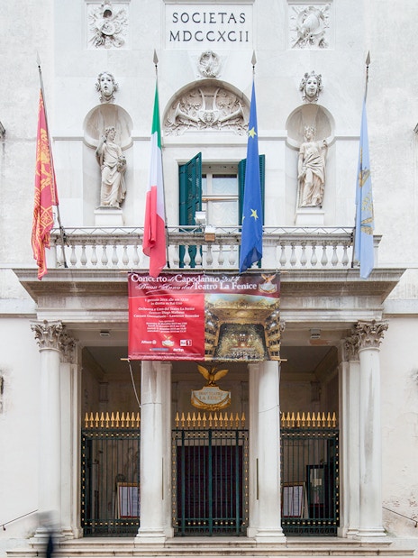 Facade of Teatro La Fenice in Venice, Italy, with flags and statues.