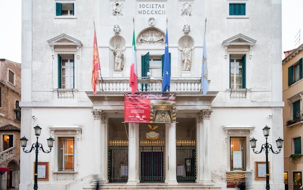 Facade of Teatro La Fenice in Venice, Italy, with flags and statues.
