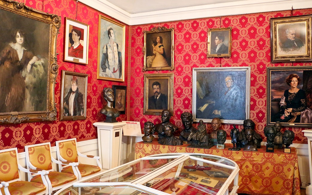 La Scala museum room with portraits and busts on red patterned walls.