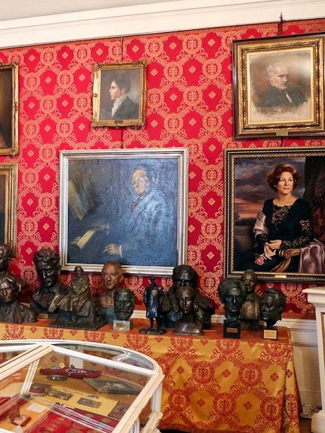 La Scala museum room with portraits and busts on red patterned walls.