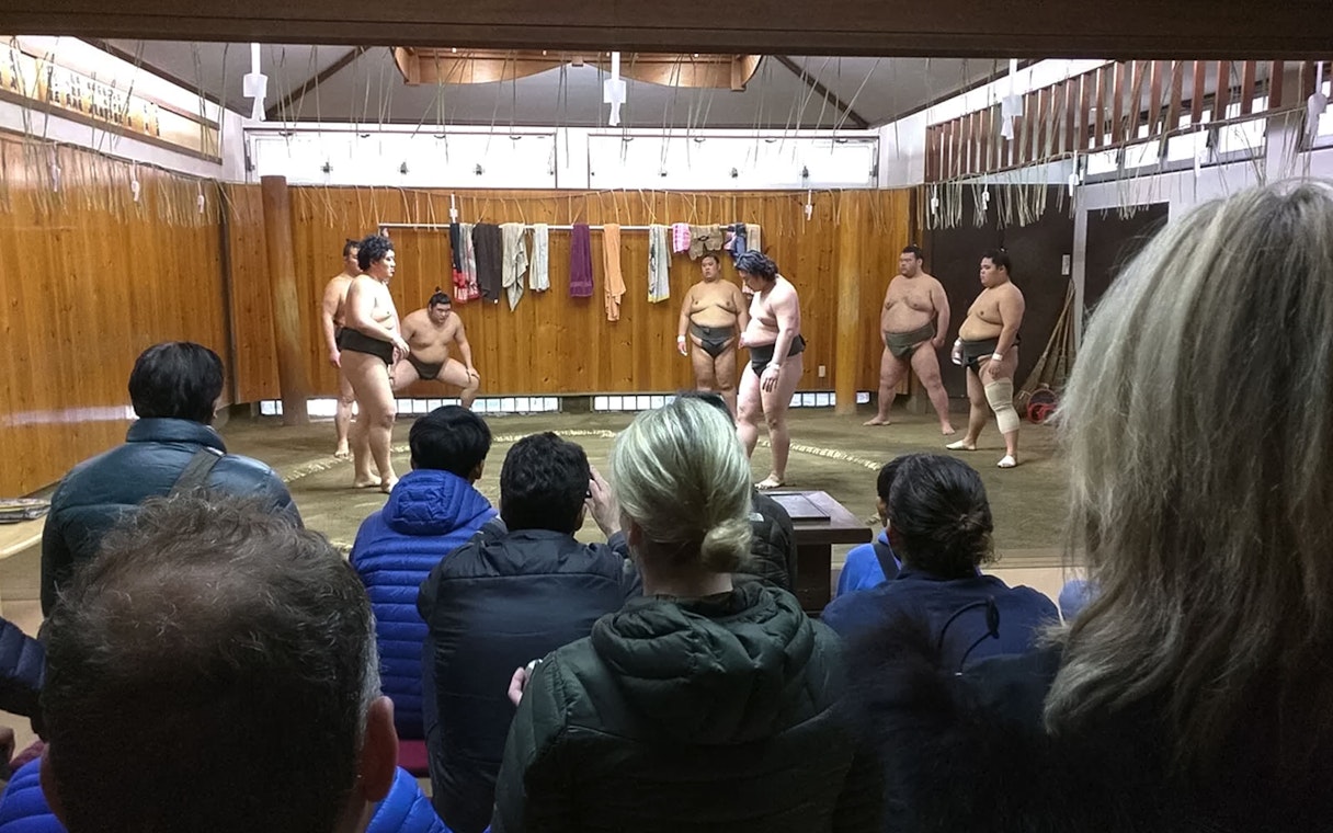 Sumo wrestlers training in a Tokyo dojo with spectators watching.