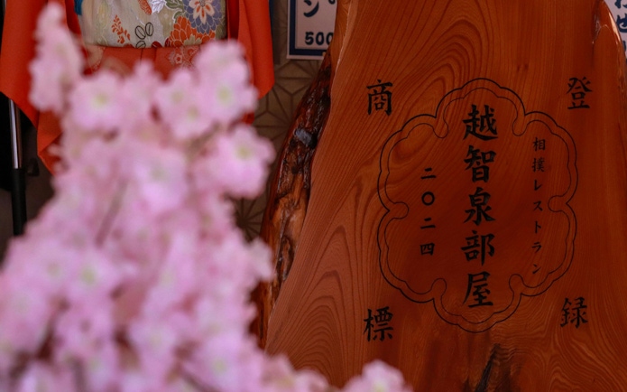 Sumo practice venue sign at Ochiizumibeya with cherry blossoms in foreground.