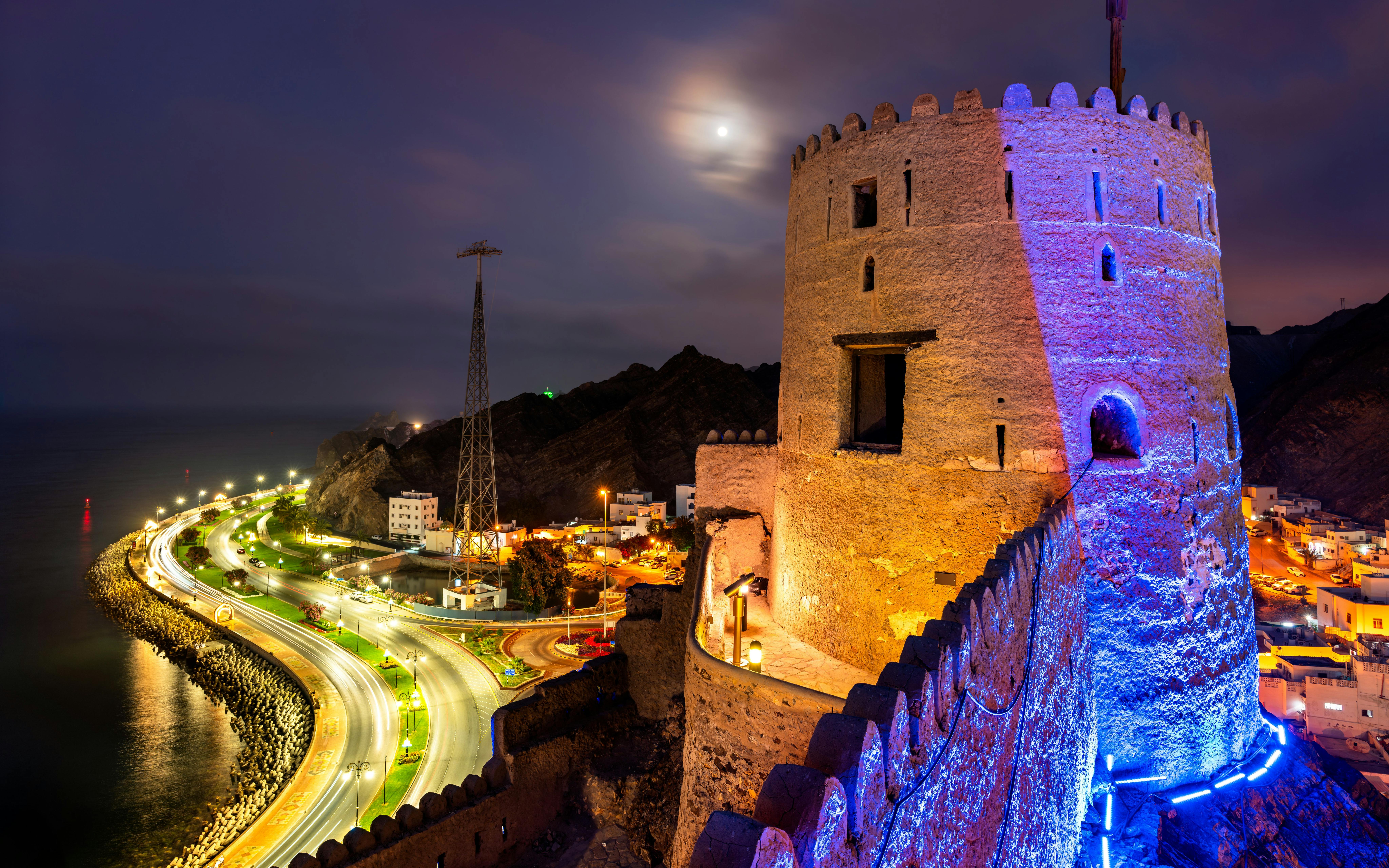 Corniche road and illuminated fort at night in Muscat, Oman.