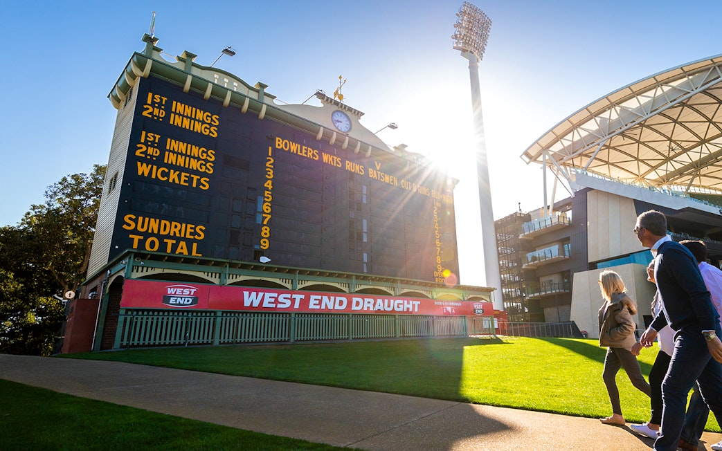 People walking past the historic scoreboard at Adelaide Oval Stadium.